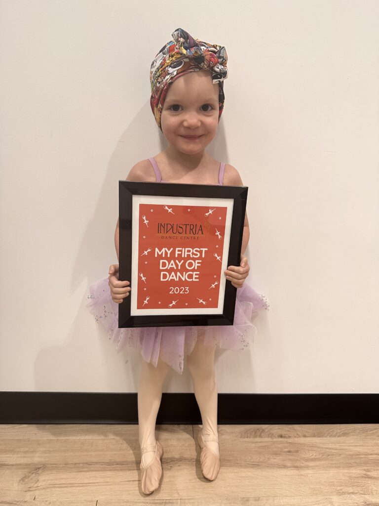 Ella wears a tutu and holds a sign that says "My first day of dance."
