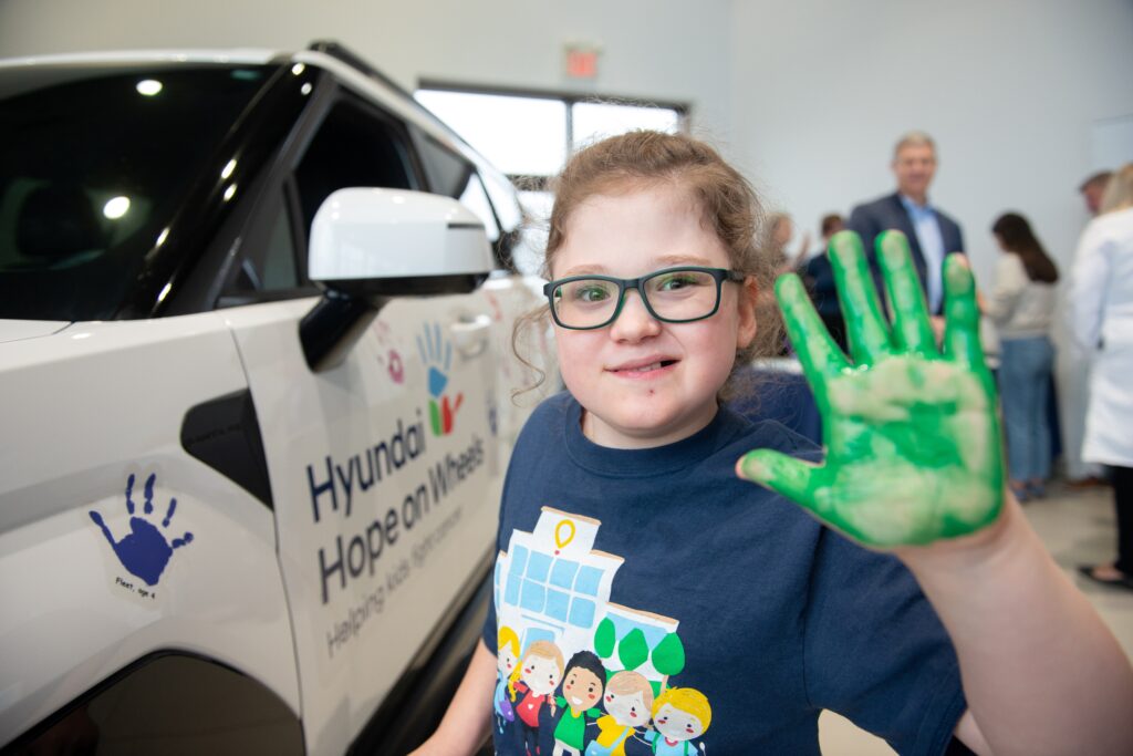 Champion Child Jack holds up hand covered in green paint and smiles
