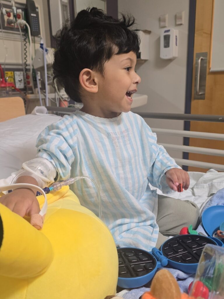 Rayan smiles and plays with toys in his hospital bed