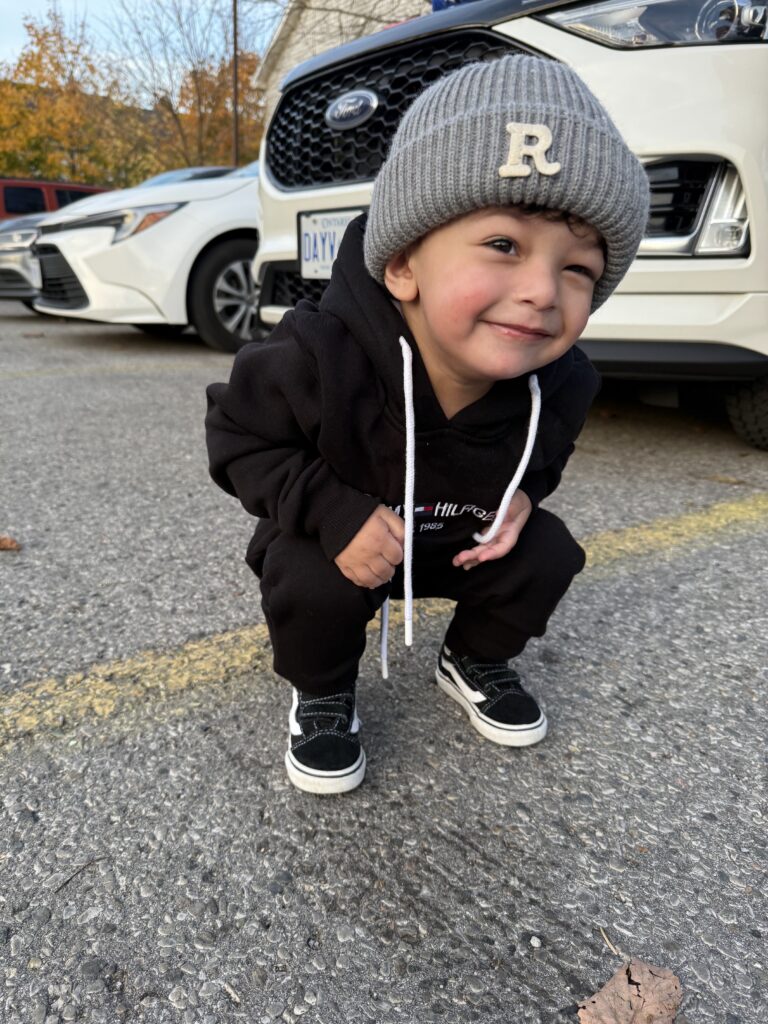 Rayan squats in a parking lot and smiles at the camera