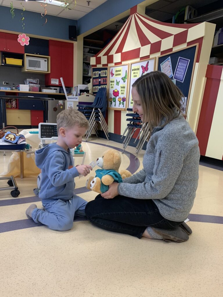Calvin and a Child Life Specialist play with a teddy bear in the hospital playroom.