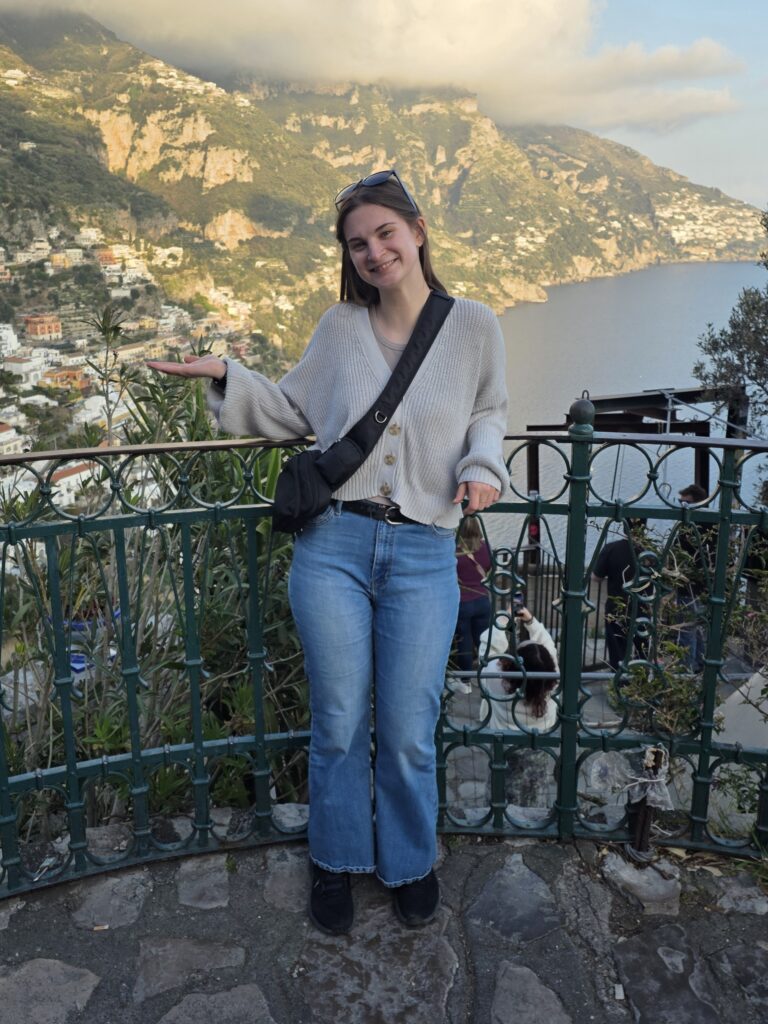 Sage standing on a balcony as an adult