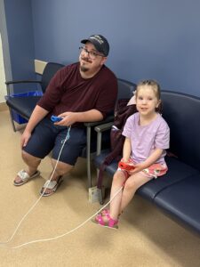 Vayle and her father Andrew play video games in a waiting room.