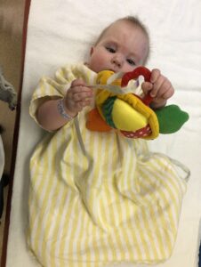 Baby Vayle in a hospital gown holding a toy.