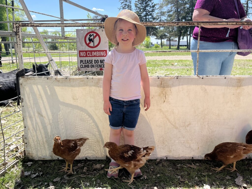 Vayle smiling in front of a fence with chickens around her feet.