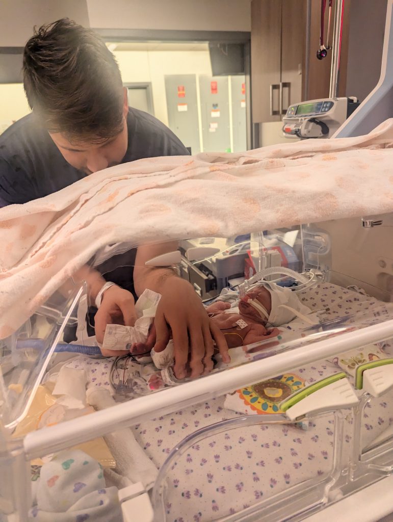 Patrick changes baby Juliette's diaper in her hospital bed in the NICU.