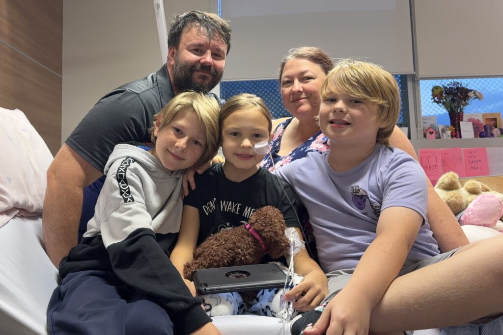 Abby sits in her hospital bed surrounded by her parents and brothers.