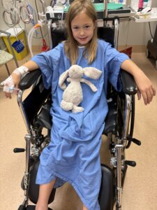 Abby sits in a wheelchair with her stuffed animal on her chest.