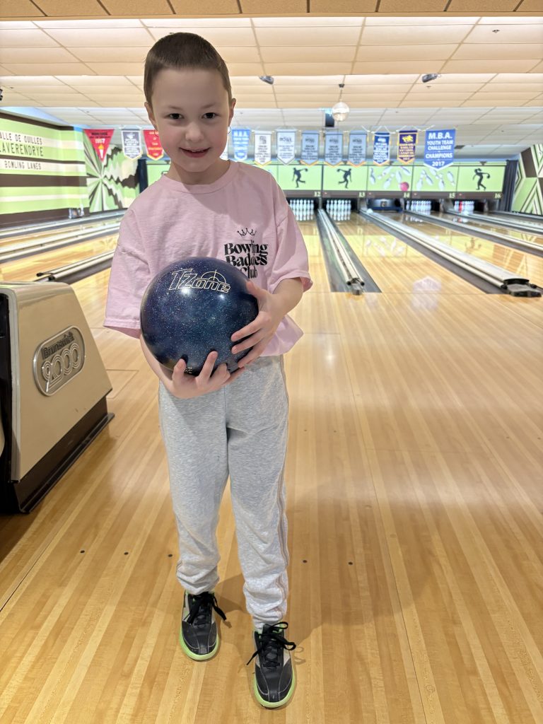 Abby holds a bowling ball in front of a bowling lane.