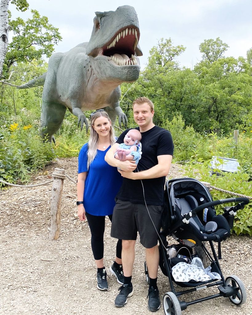 Kelsey and Mark with Paxton in front of a dinosaur at the zoo.