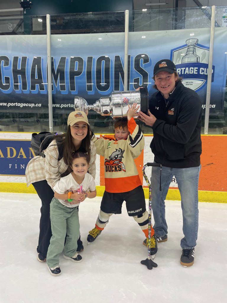 Gordie holds a hockey trophy over his head while standing on the rink with his parents Sarah and Ryan and younger sister Molly.