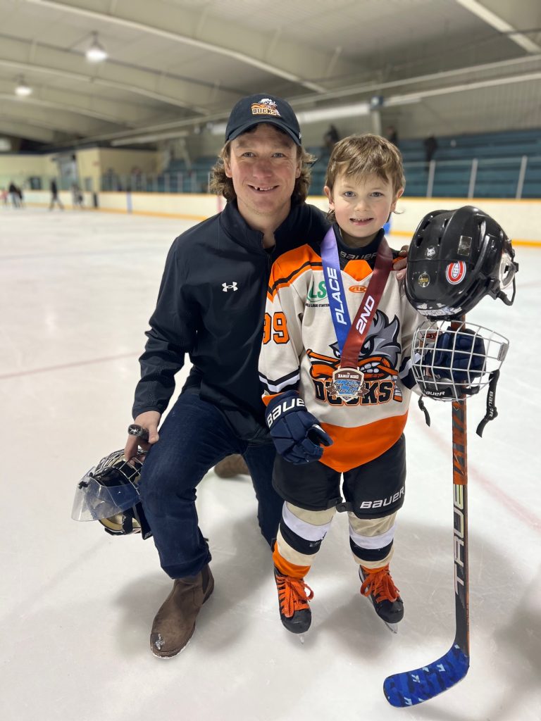 Gordie dressed in his hockey gear, standing on the rink with his dad Ryan.